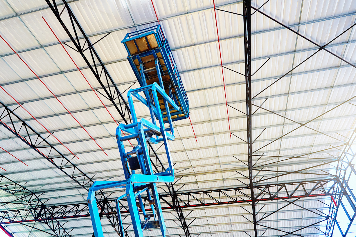 Pantographic mobile crane rises towards the roof of a warehouse under construction